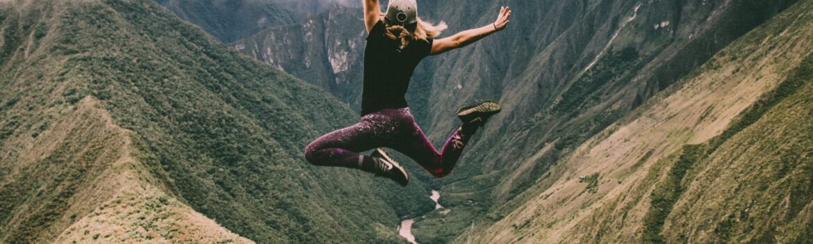 woman jumping on green mountains